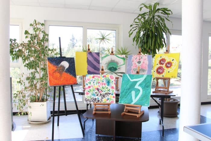exposition de tableaux créés par les étudiants. 7 toiles sur chevalet, au milieu d'une pièce contenant de la végétation.